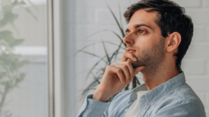 a person sitting in front of a window with their hand on their chin